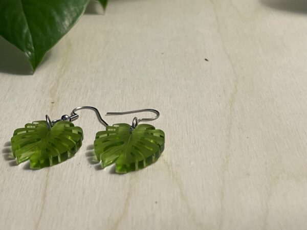 Acrylic moss green monstera leaf dangle earrings lying flat