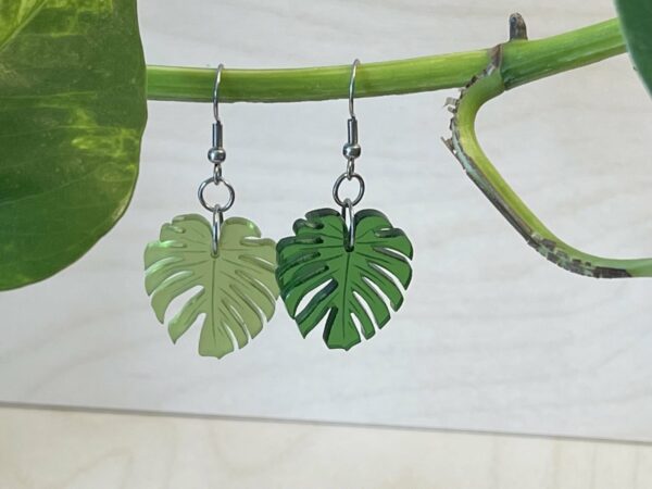 Acrylic monstera leaf dangle earrings in two shades of green hanging on a branch
