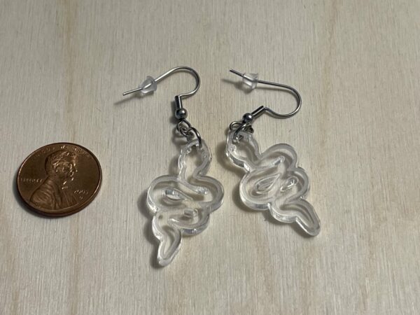 Acrylic snake dangle earrings, shown for size next to a penny, in the color clear